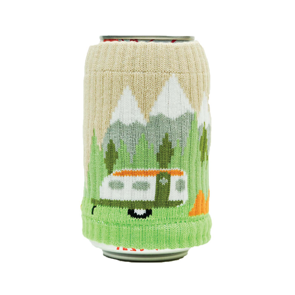 A can covered with a knitted drink sleeve that depicts a camper in a mountain scene