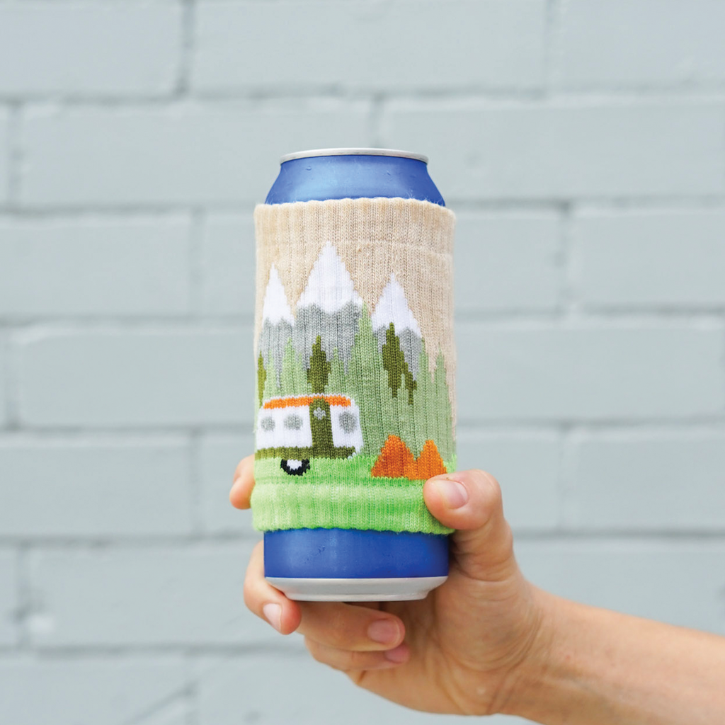 A can covered with a knitted drink sleeve that depicts a mountain scene
