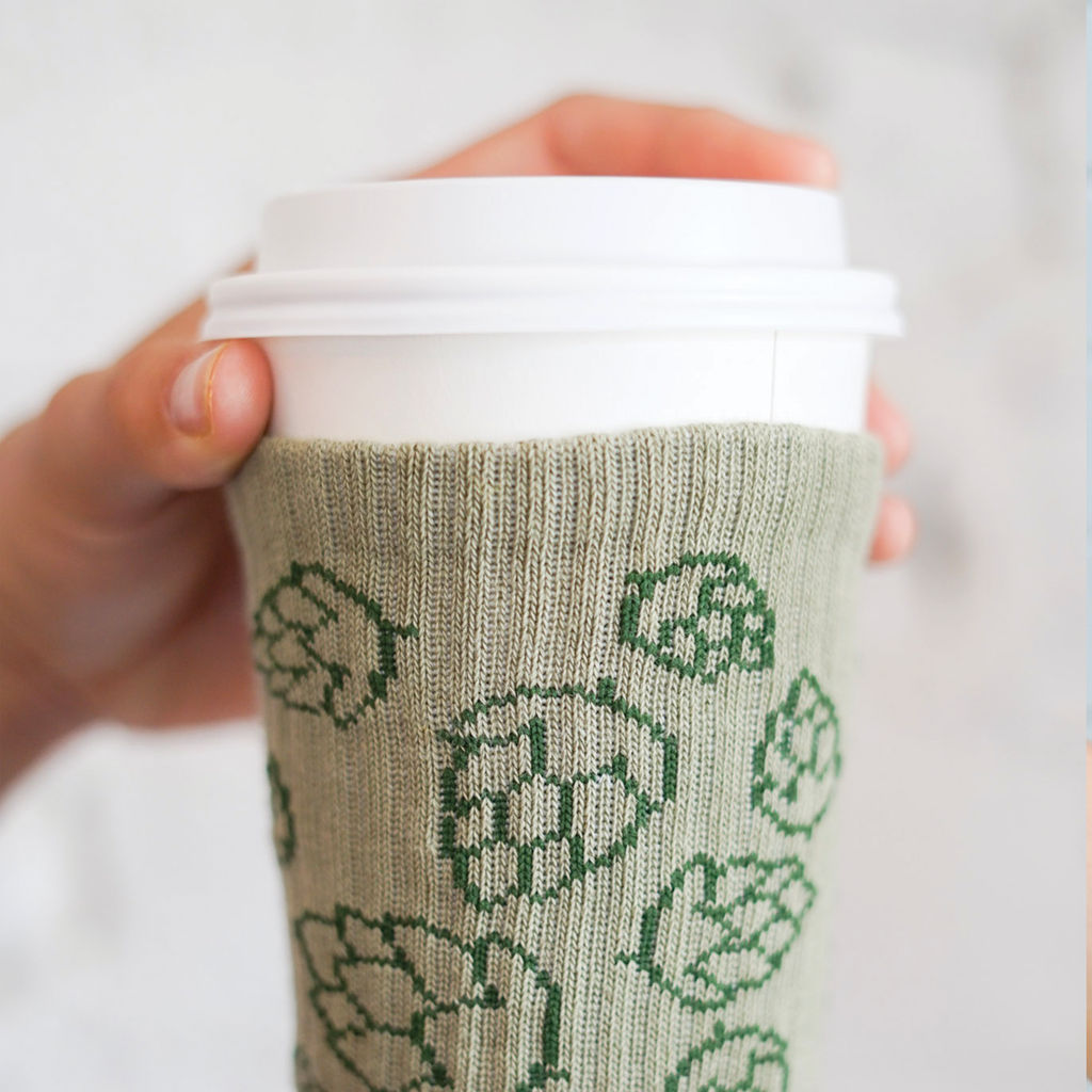 Upclose of a to-go coffee cup covered with a knitted drink sleeve with a hops beer design