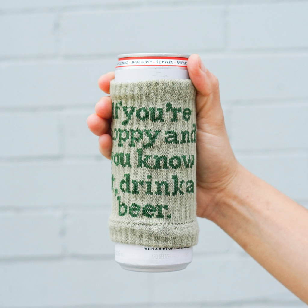 A beer can covered with a knitted drink sleeve with text