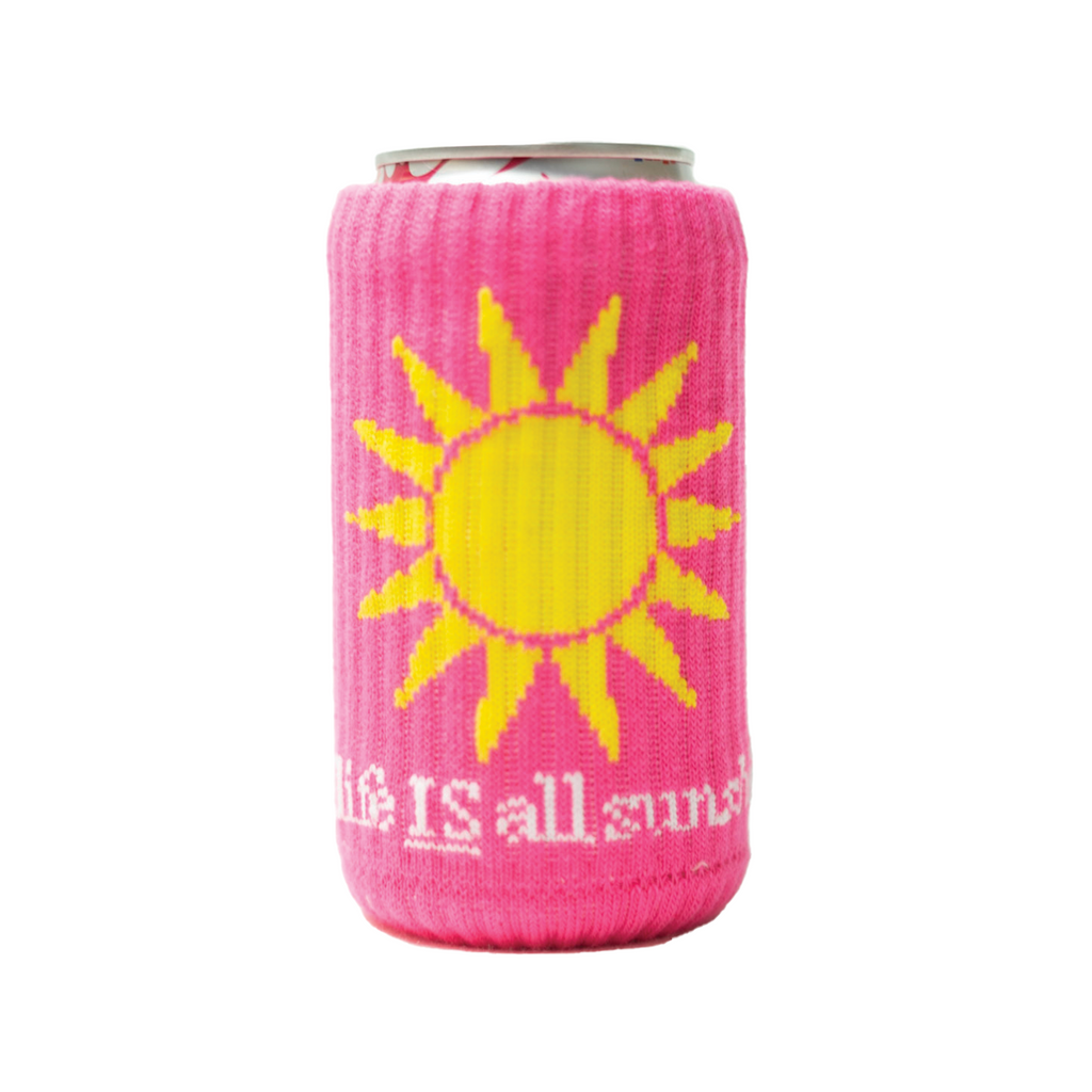 A can covered with a pink knitted drink sleeve that depicts a bright yellow sun and text